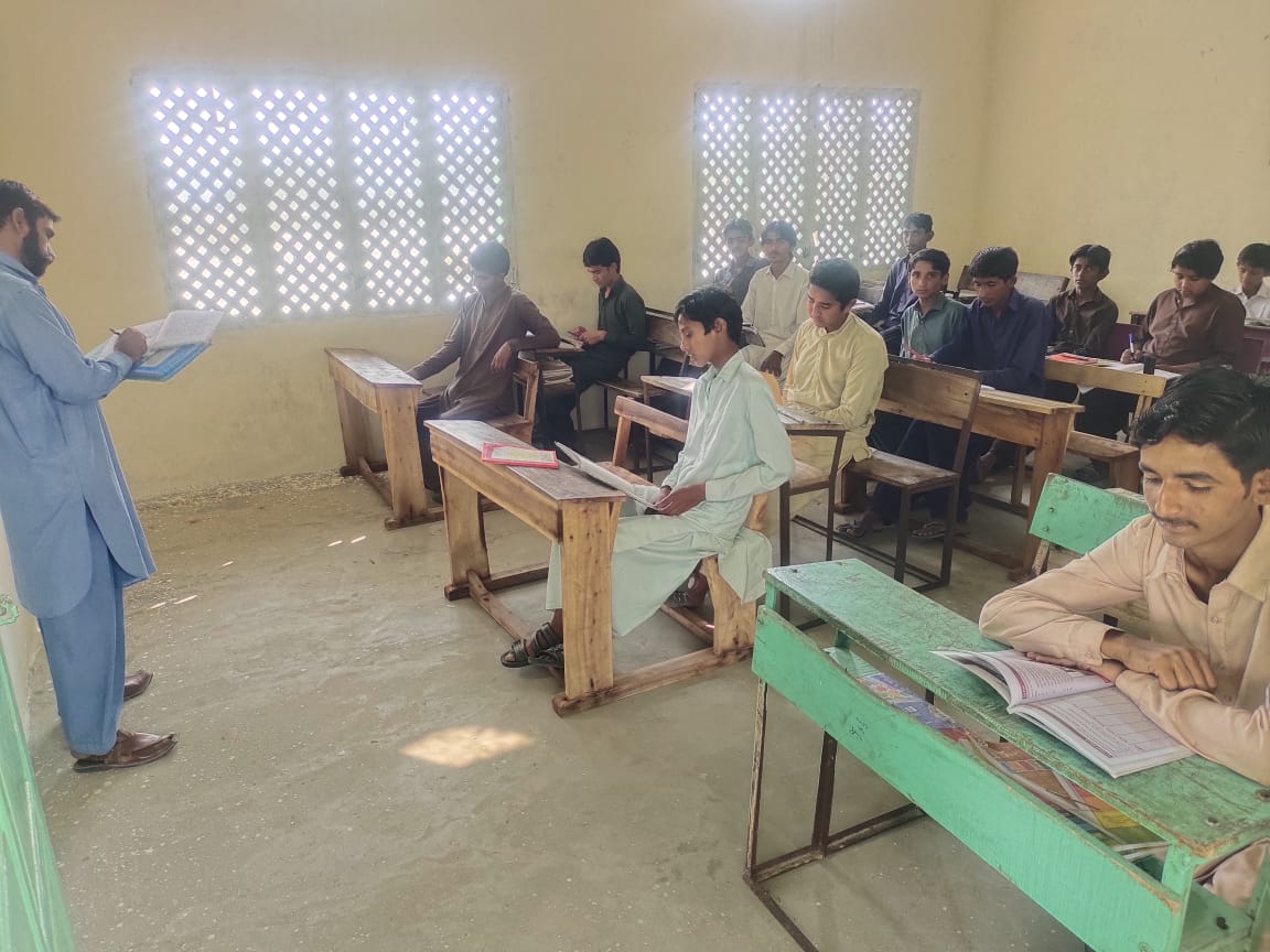 Teacher taking attendance as students study at wooden desks